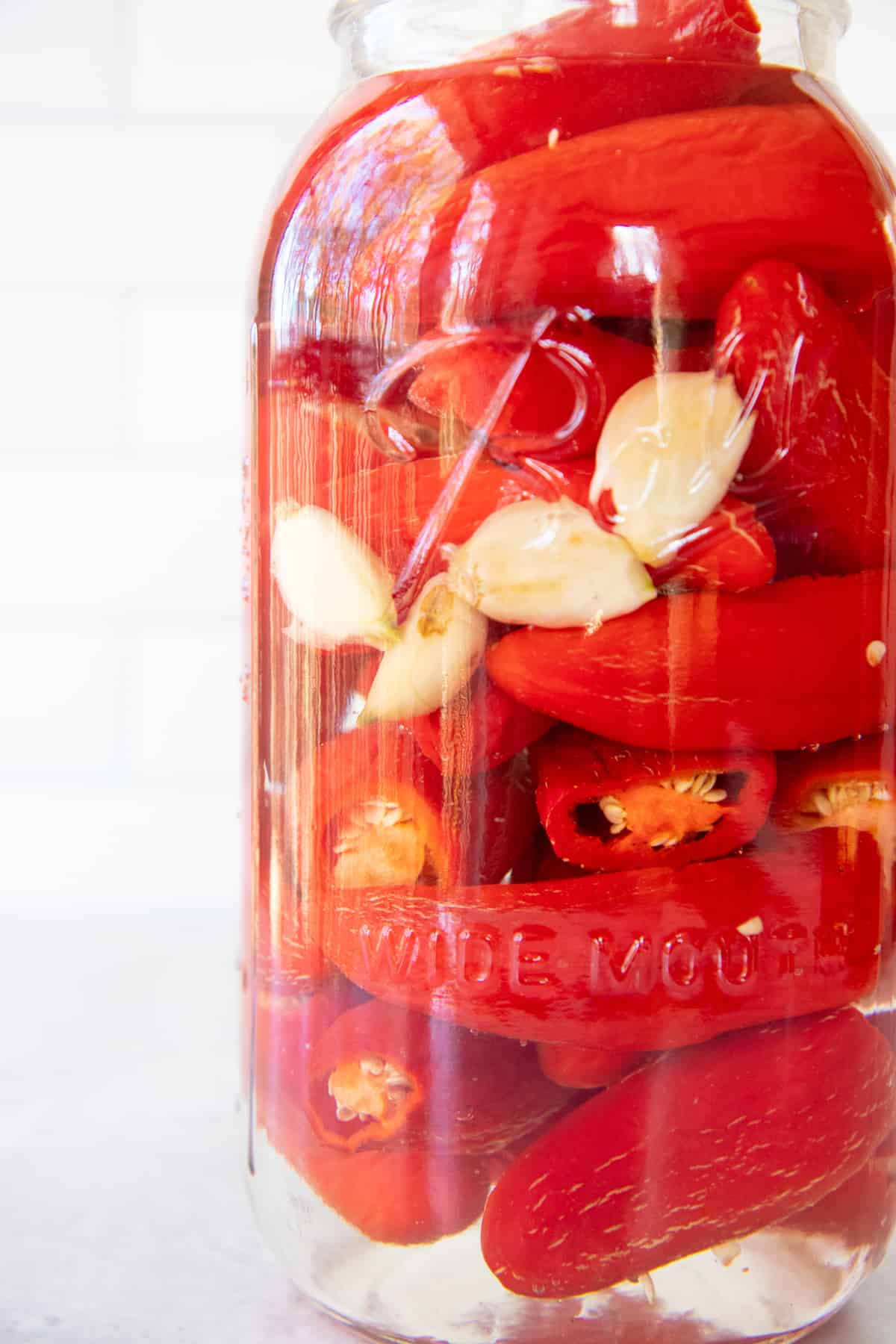 Close up of red peppers and garlic fermenting in a glass jar.