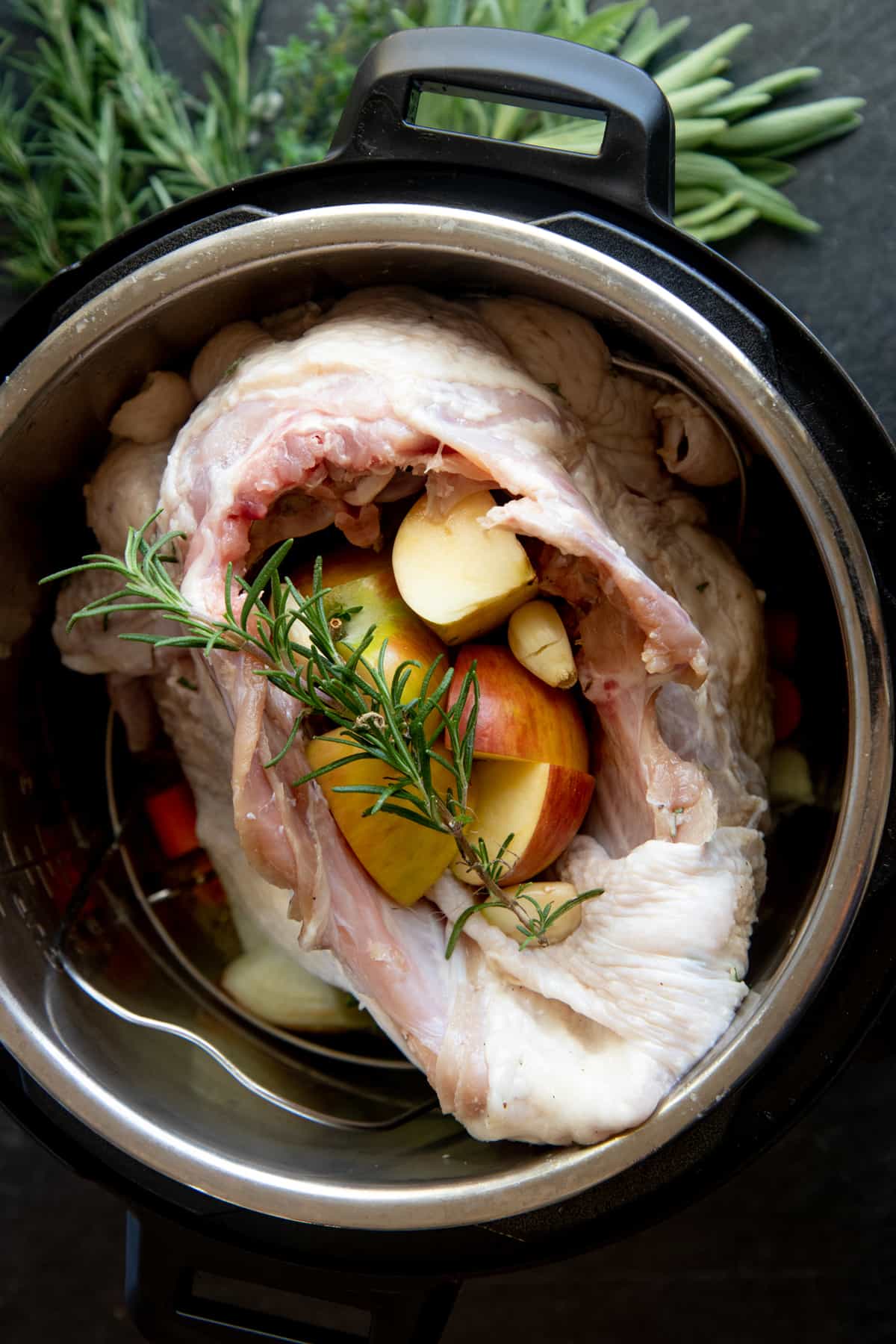 A turkey breast stuffed with aromatics sits in the basin of an electric pressure cooker, ready to be cooked.