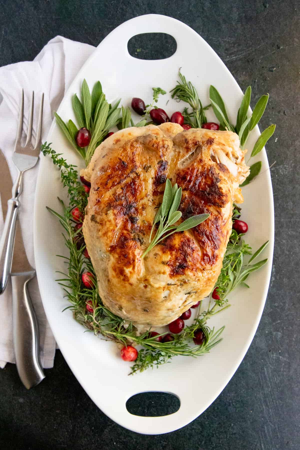 Cooked Instant Pot turkey breast on a bed of herbs and cranberries on a white platter.