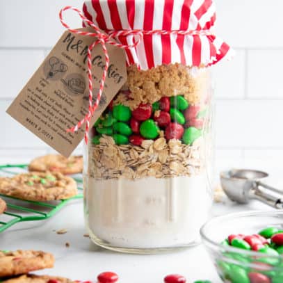 A mason jar filled with even layers of dry ingredients for cookie mix in a jar, topped with fabric, a baking instructions tag, and baker's twine.