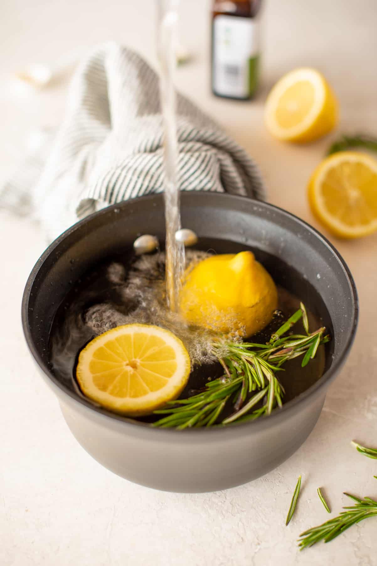 Water pours into a small saucepan holding rosemary and a halved lemon.