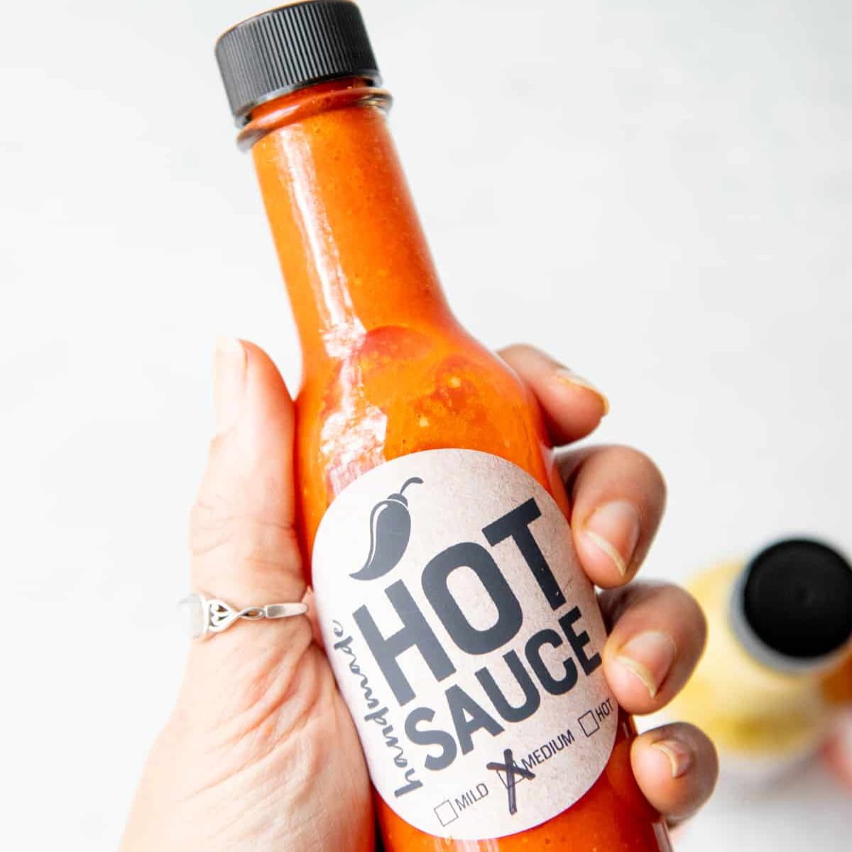 A hand holds a bottle of homemade hot sauce with a label
