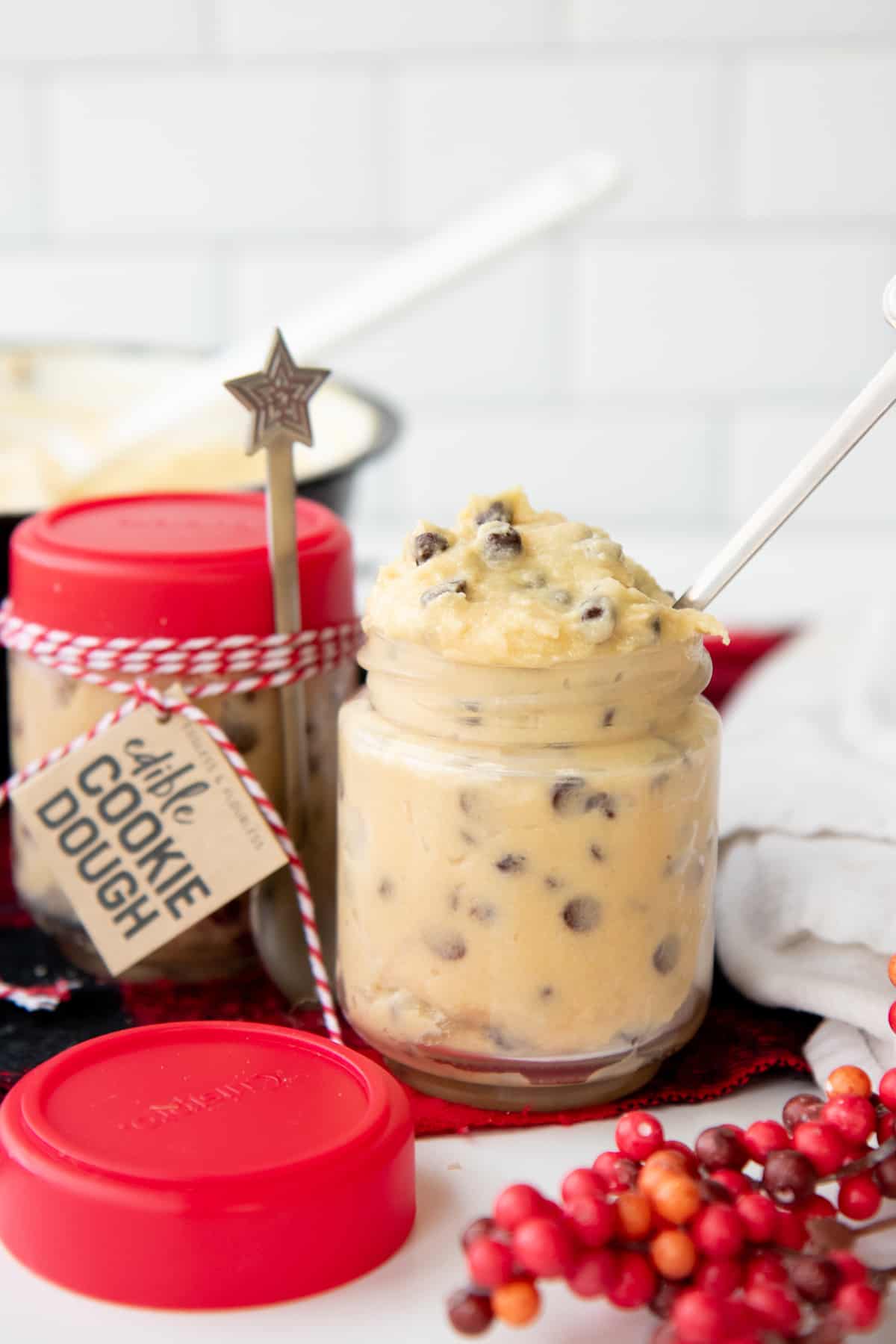 An open jar of edible cookie dough with a white spoon in it sits in front of a packaged jar of the dough.