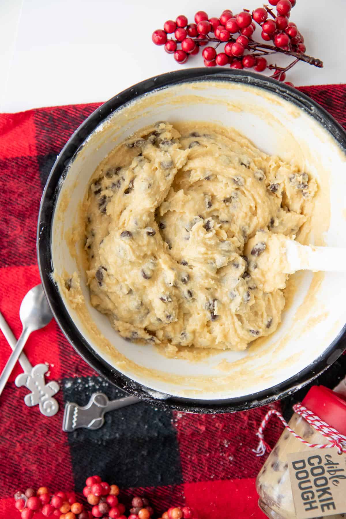 A mixing bowl full of edible chocolate chip cookie dough sits on a red and black plaid placemat.