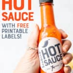 A hand holds out a bottle of red hot sauce. A text overlay reads "Homemade Hot Sauce with Free Printable Labels!"