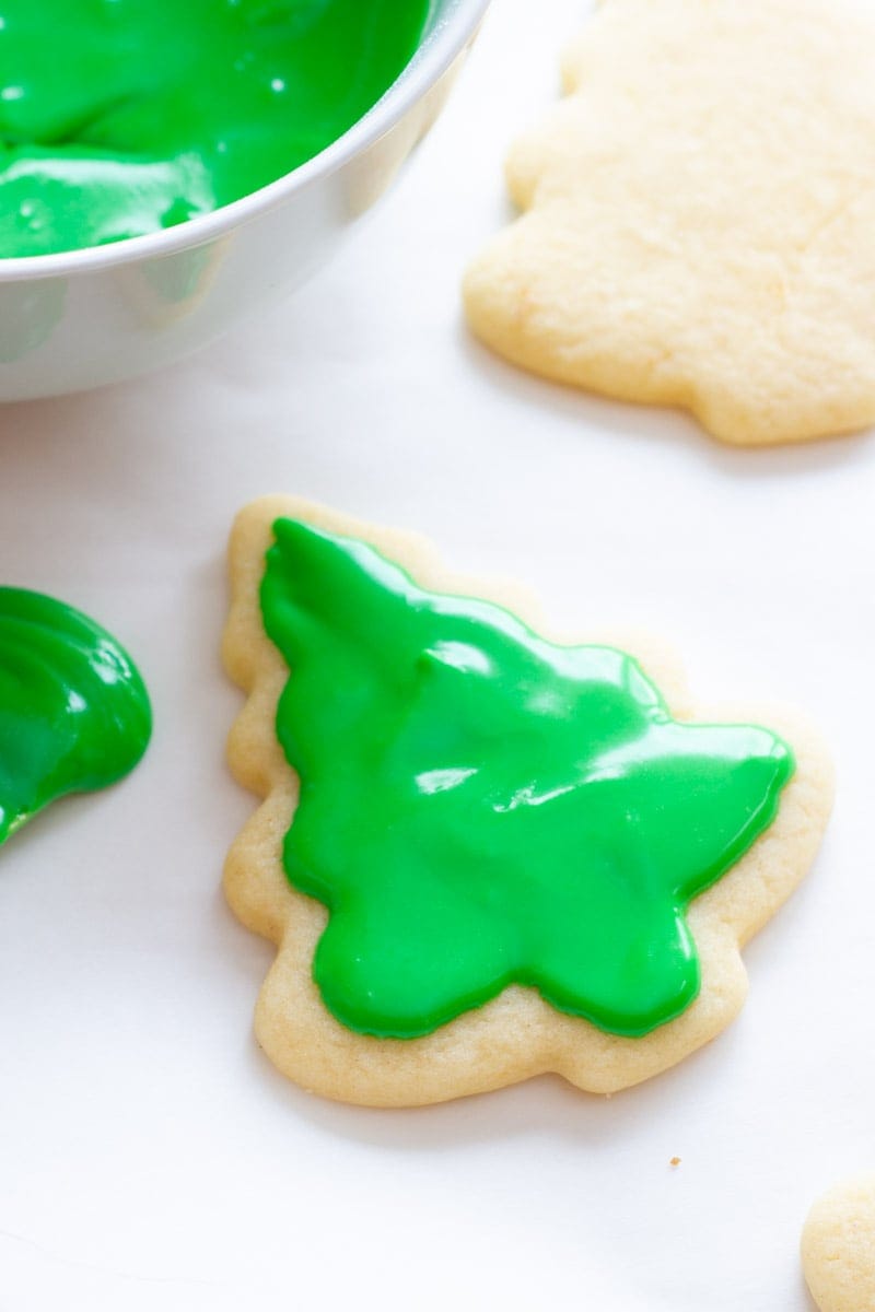 A tree-shaped cookie spread with green sugar cookie icing sits next to a bowl of frosting.