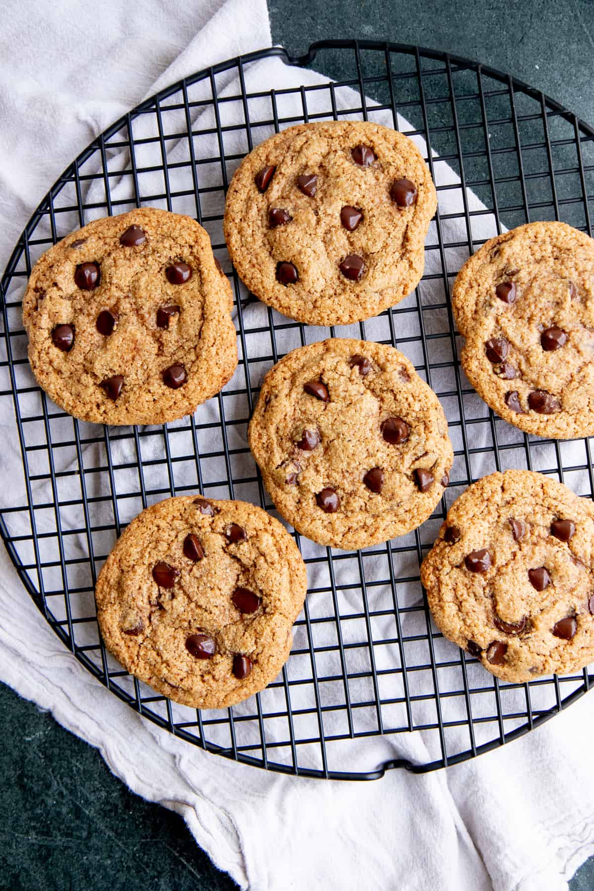 Six chocolate chip cookies sit on a round wire cooling rack.