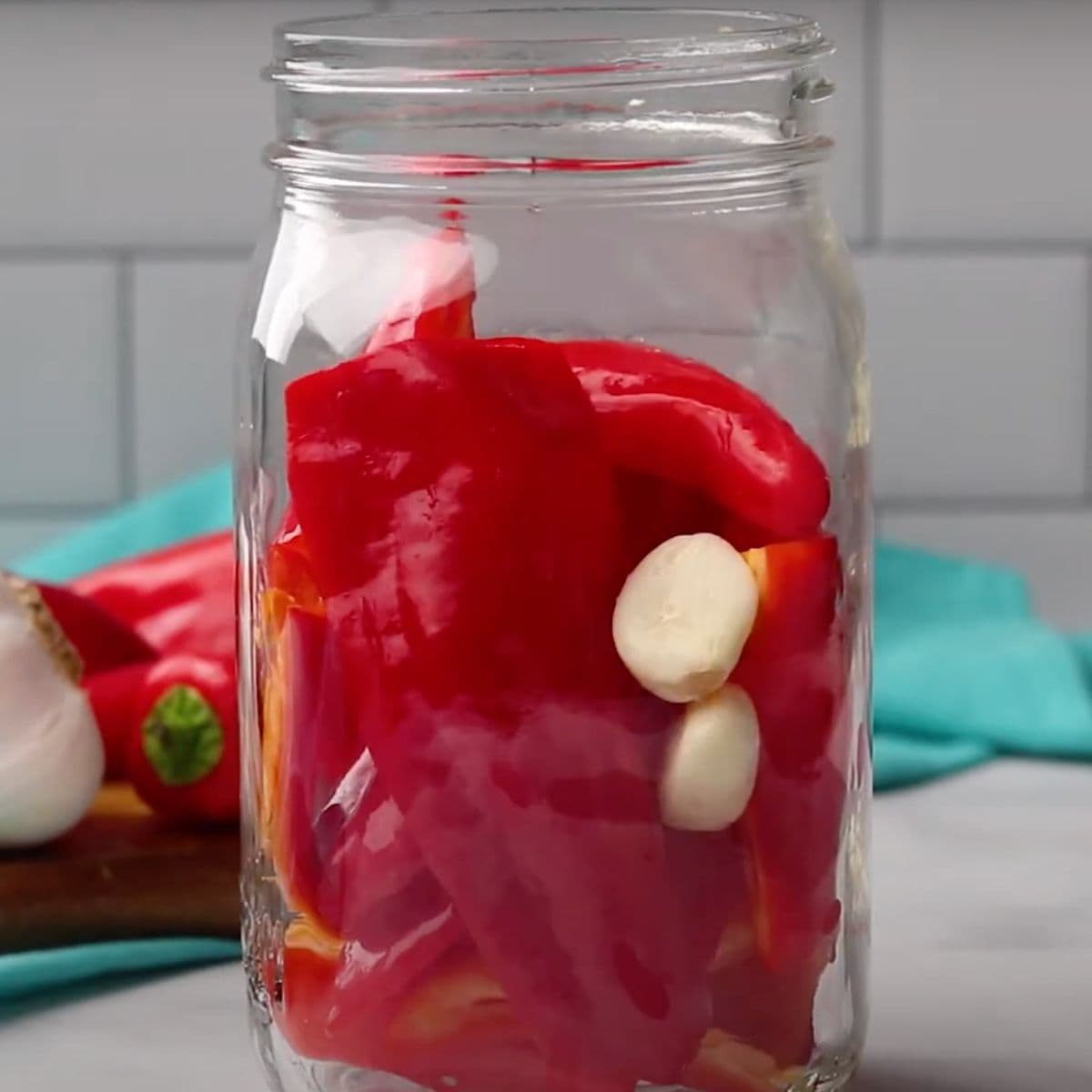 Peppers in garlic in a clear glass canning jar on a gray countertop