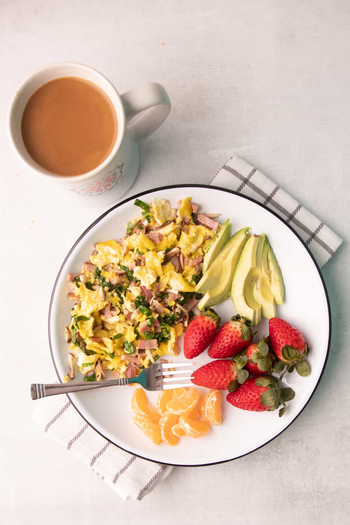Breakfast on a white plate: egg scramble, fruit, and avocado. A mug sits next to the plate.