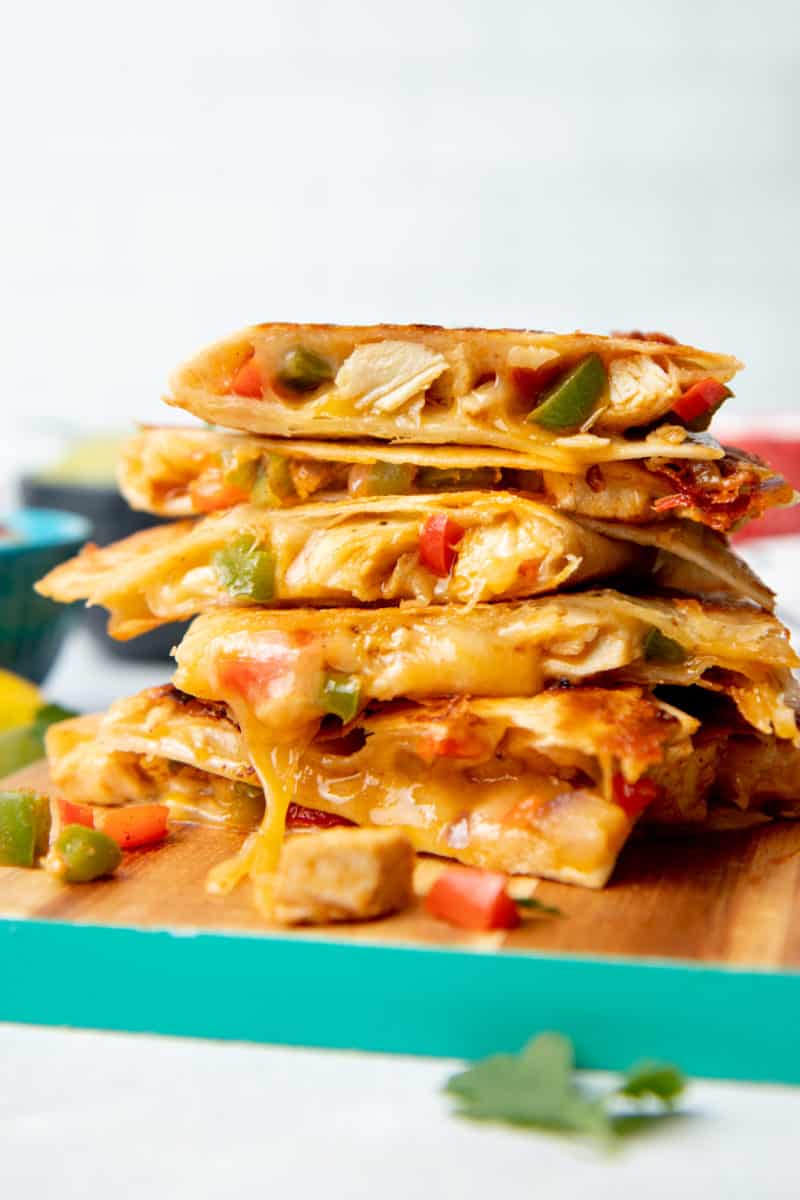 Chicken quesadillas are stacked on a wooden cutting board. The board has a teal edge.
