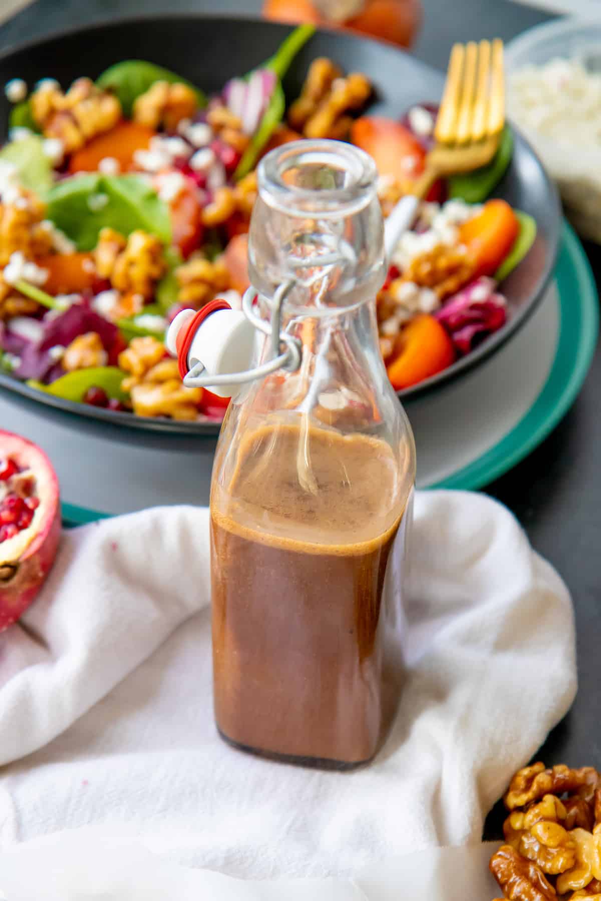 A bottle of maple vinaigrette sits in front of a bowl of salad.