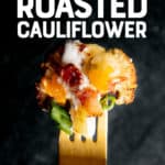 A gold fork holds a bite of loaded roasted cauliflower in front of a dark background. A text overlay reads "Loaded Roasted Cauliflower."