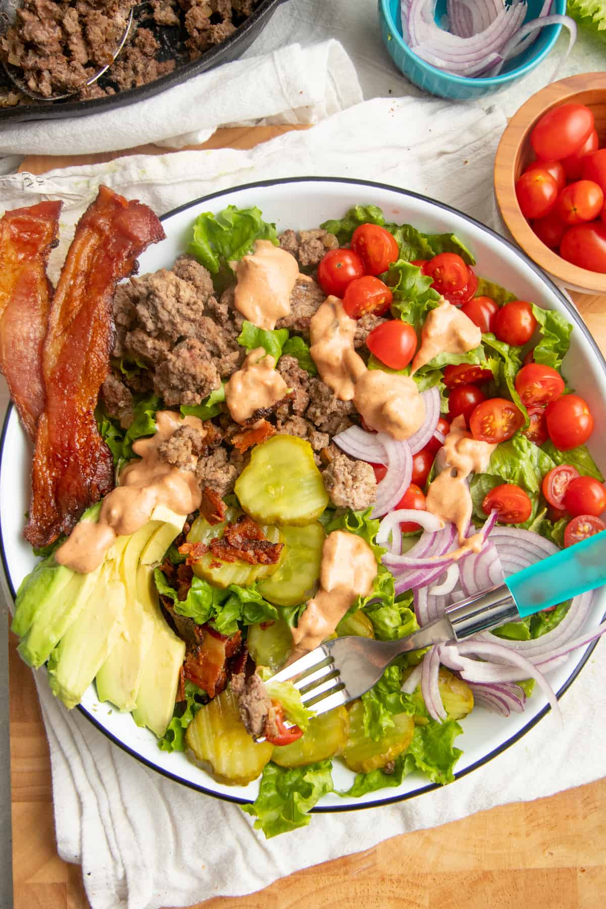 A fork with a blue handle rests in a large bowl filled a loaded burger bowl salad.