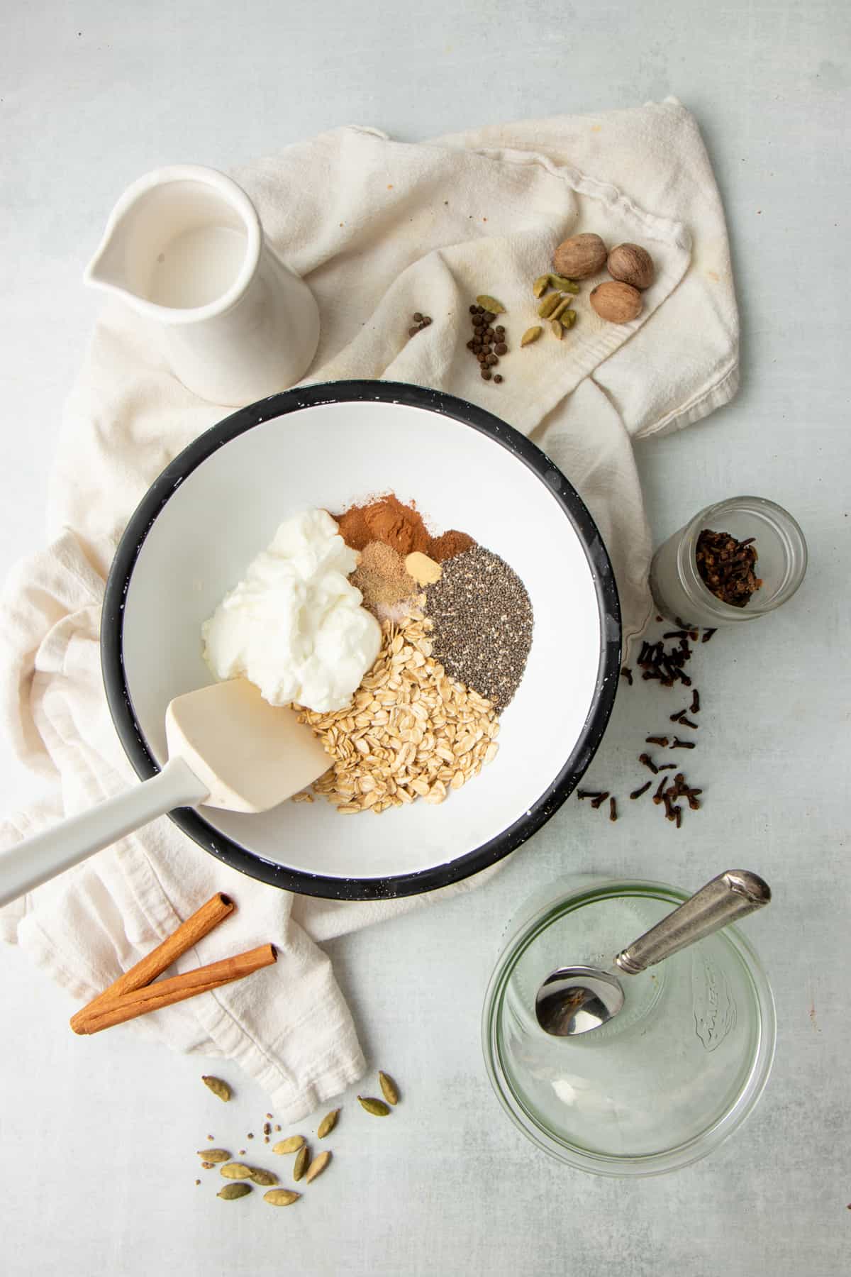 A white rubber spatula sits in a white mixing bowl full of oatmeal, chia seeds, Greek yogurt, and other ingredients.