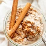 Two cinnamon sticks sit on top of a jar of chai overnight oats.