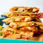 Chicken quesadillas are stacked on top of a wooden cutting board.