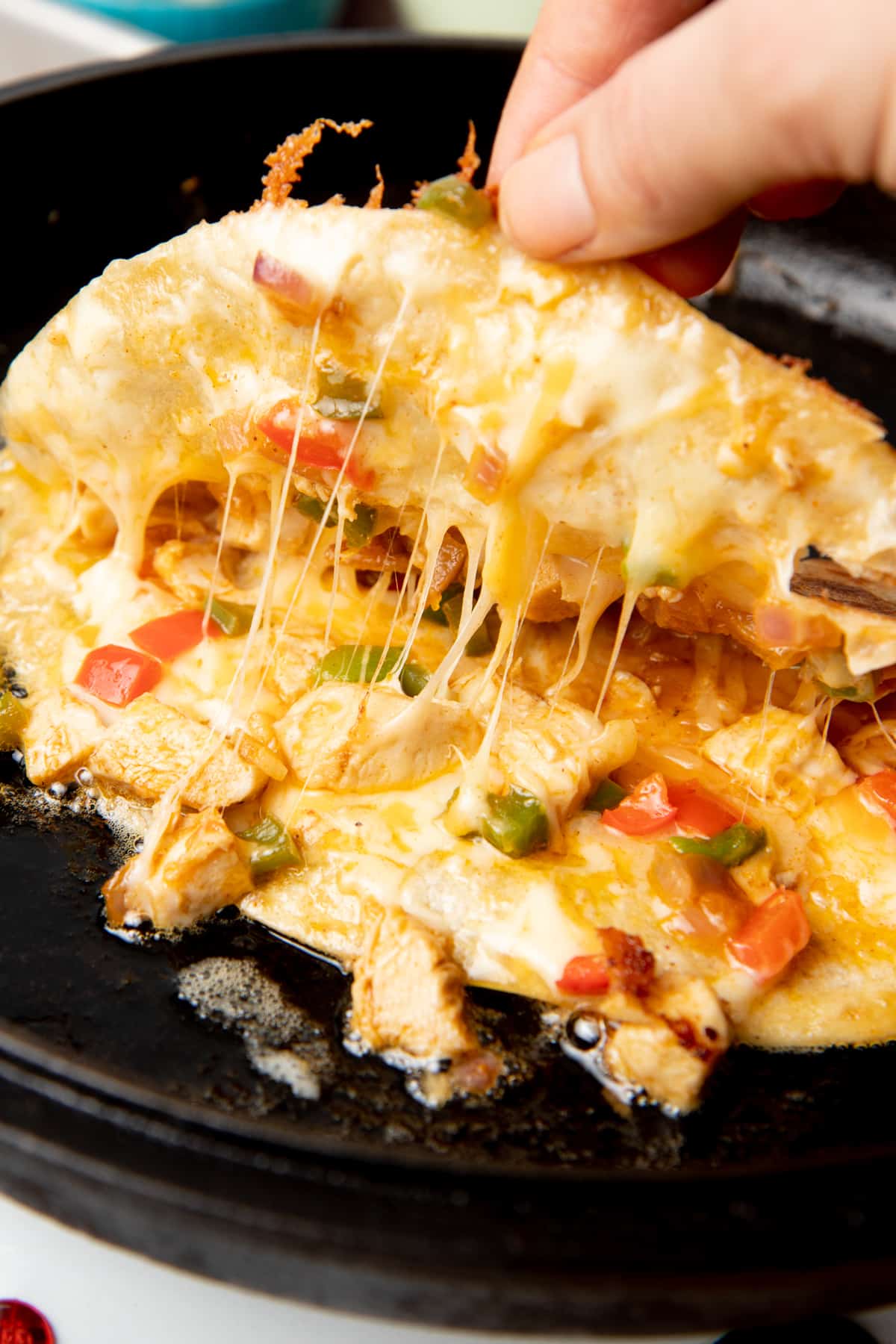 A hand lifts the top of a folded quesadilla. Chicken, peppers, and cheese are inside.