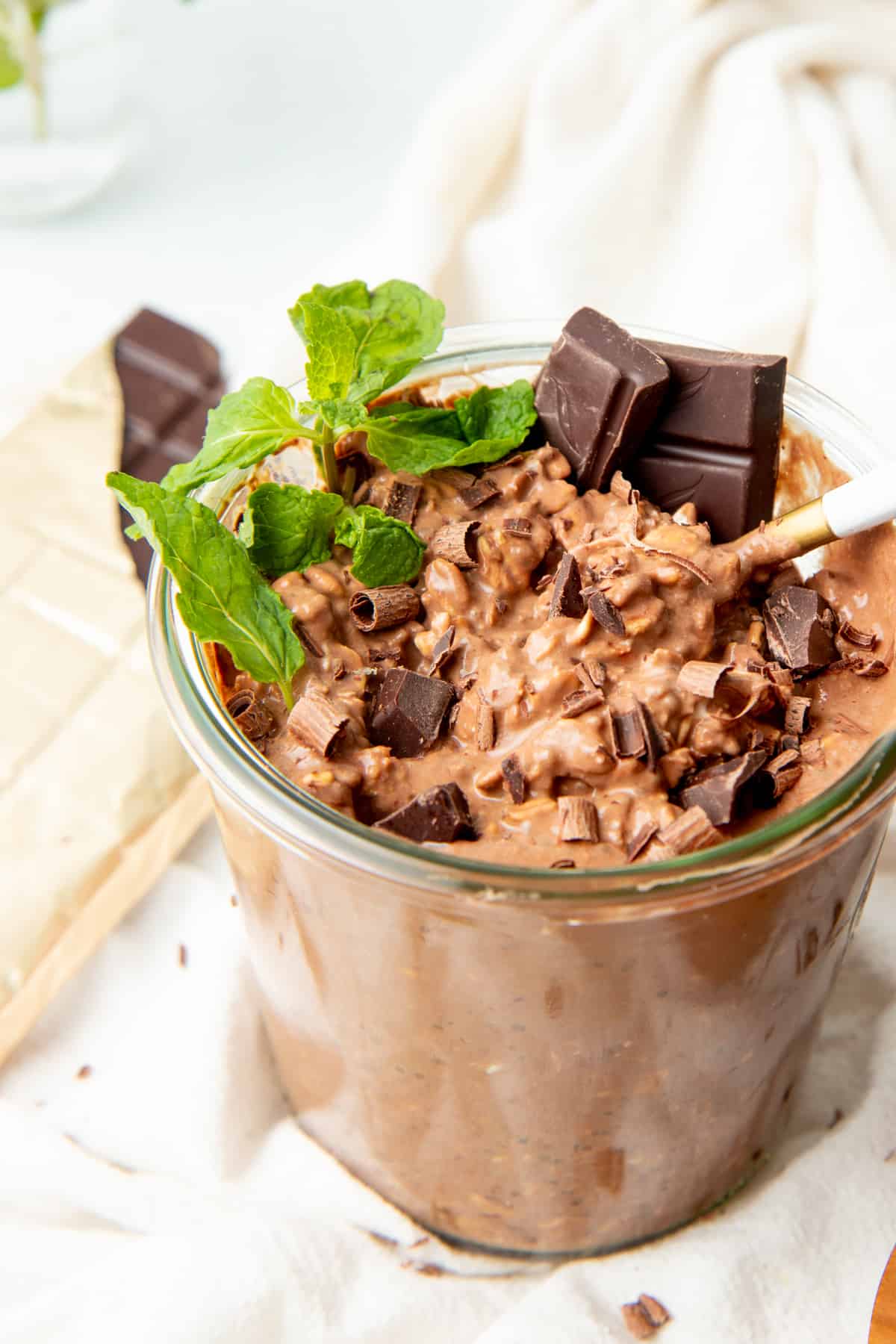 A glass jar is filled with chocolate overnight oats. Mint leaves top the oats.