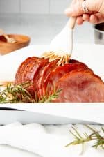 A hand bastes ham with a white brush. The dish sits on a white tablecloth.