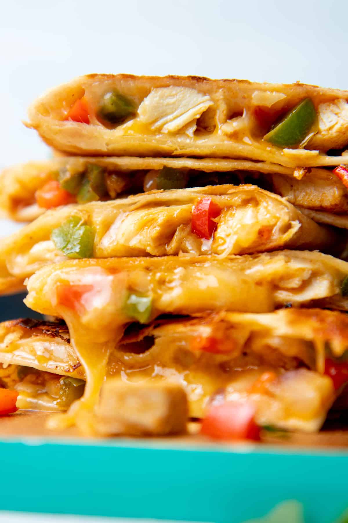 Stack of quesadilla slices filled with chicken, peppers, and cheese. The stack sits on a teal-edged cutting board.