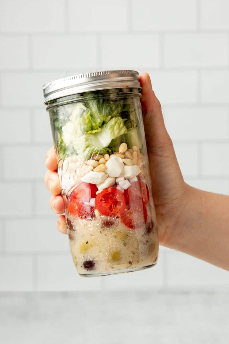 A hand holds a white-capped mason jar filled with an Italian chopped mason jar salad.