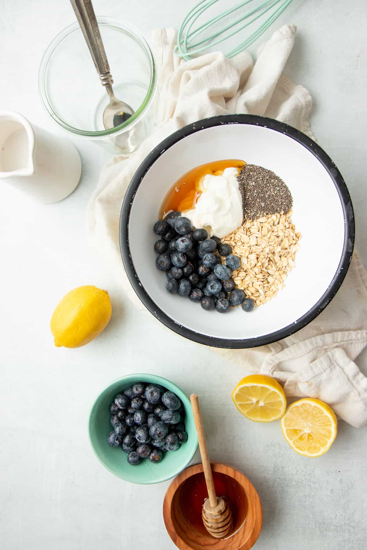 A mixing bowl filled with blueberries, oats, Greek yogurt, chia seeds, and other ingredients sits next to a halved lemon.