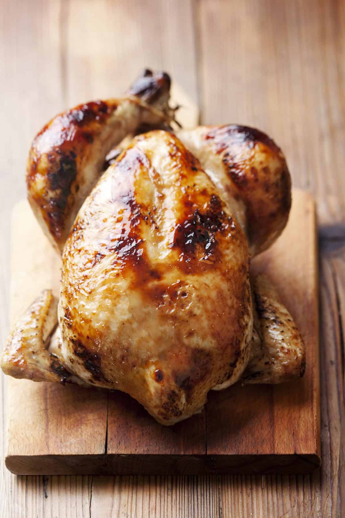 A rotisserie chicken sits on a wooden cutting board.