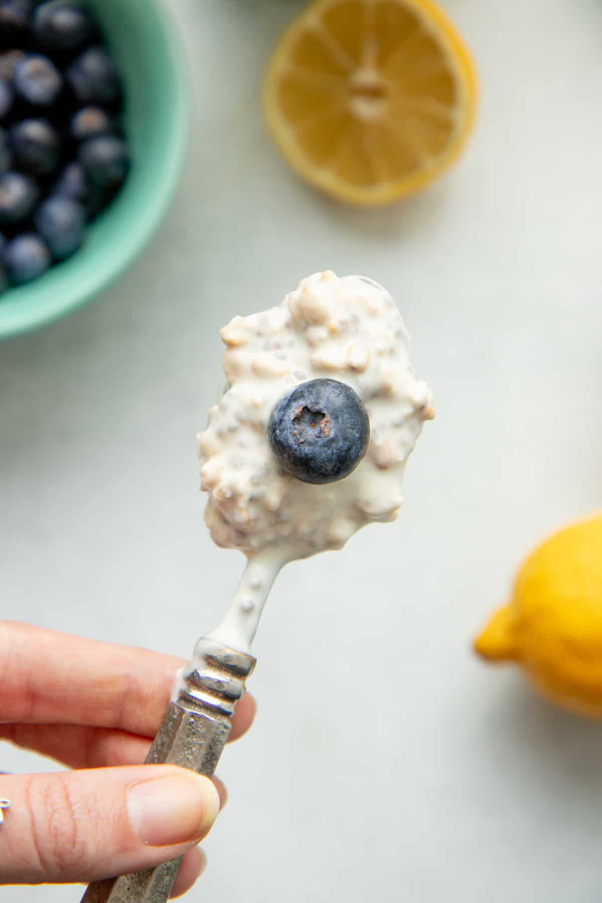 A spoon holding a bite of overnight oats is topped with a whole blueberry.