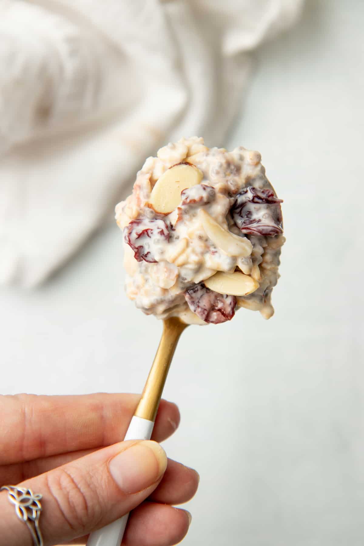 A hand holds a spoon loaded with overnight oatmeal.