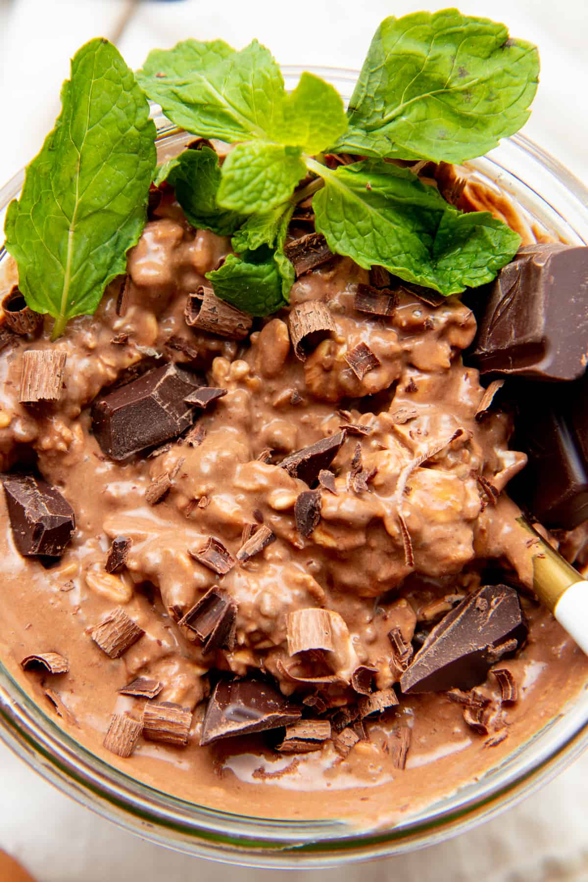 Overnight oats fill a glass jar. Chopped chocolate and mint leaves accent the top.