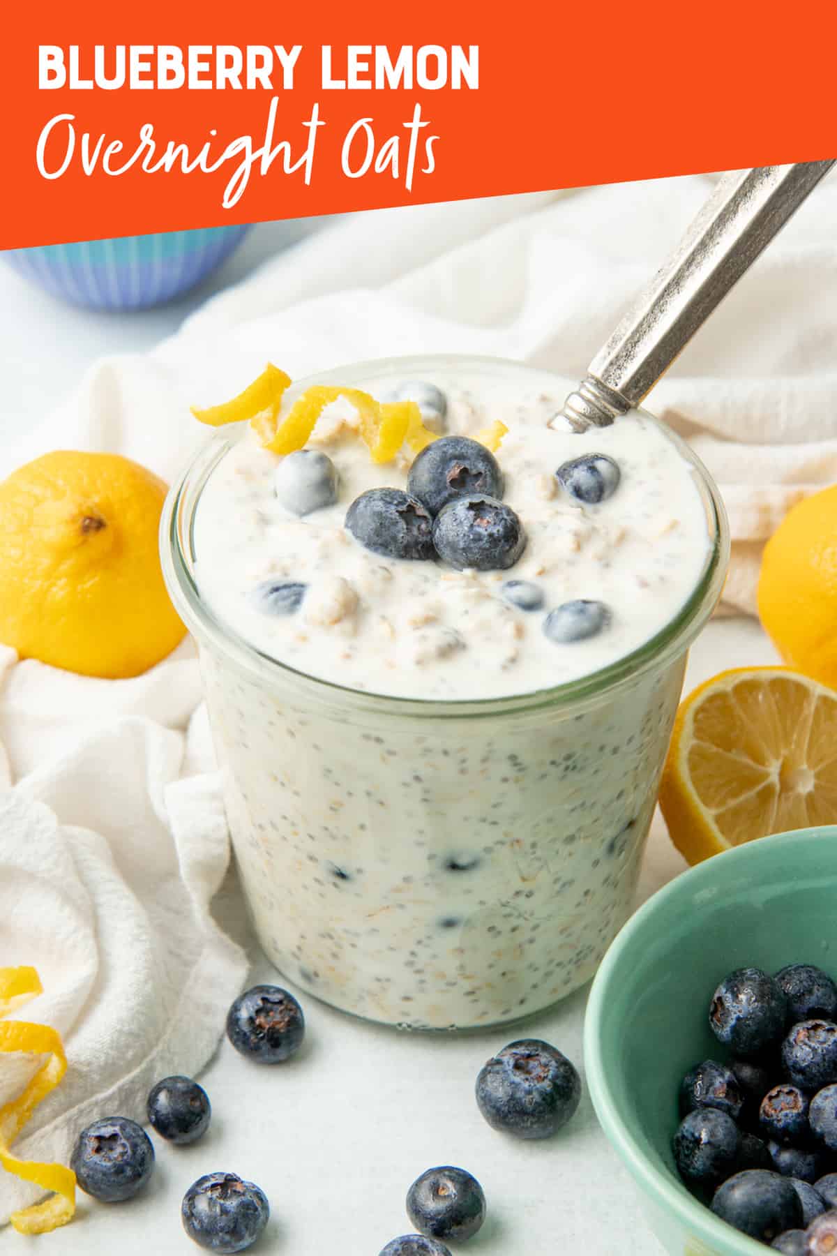 A spoon sits in a jar of blueberry overnight oats. Lemons surround the jar.