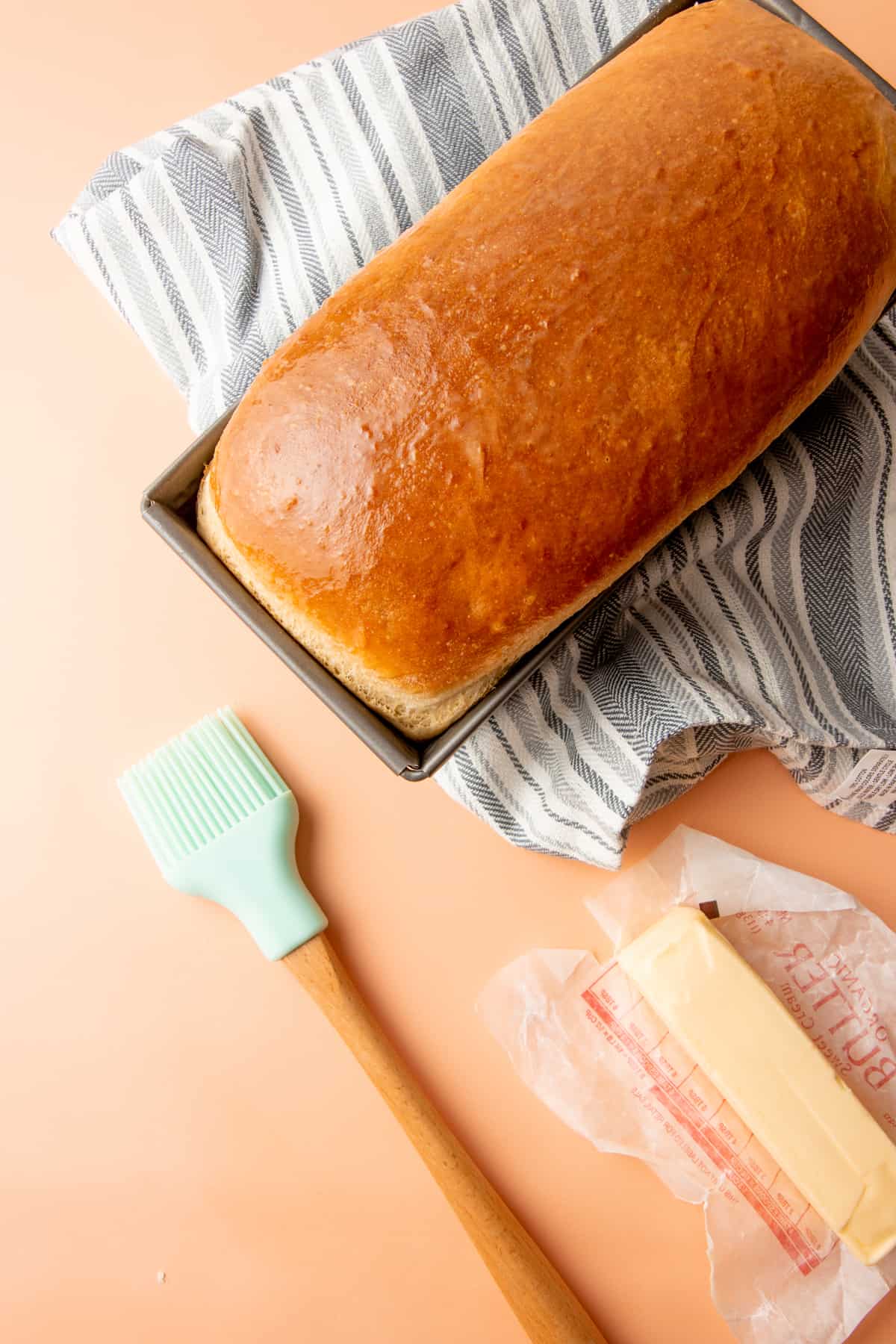 A brush brushes butter on a baked loaf of bread.