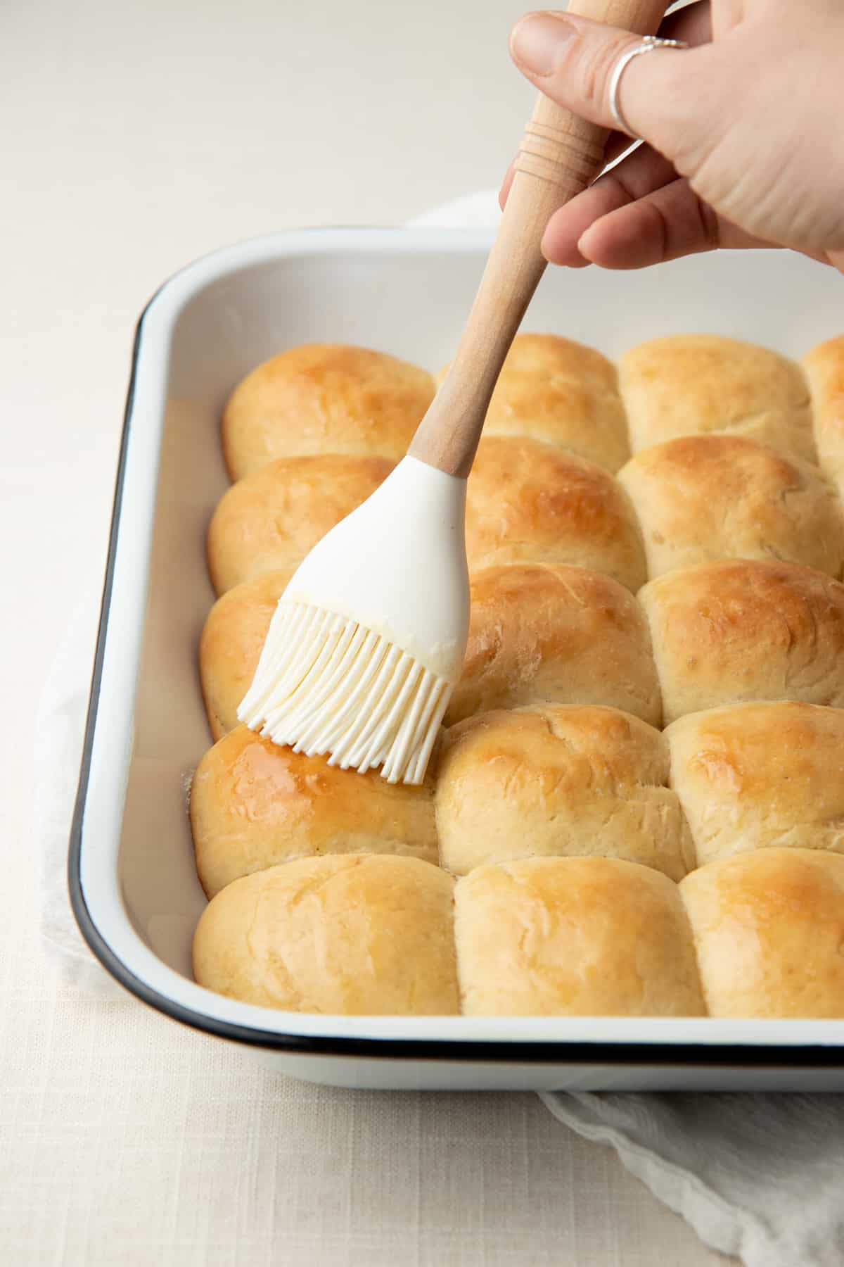 A hand brushes a pan of baked bread with butter.