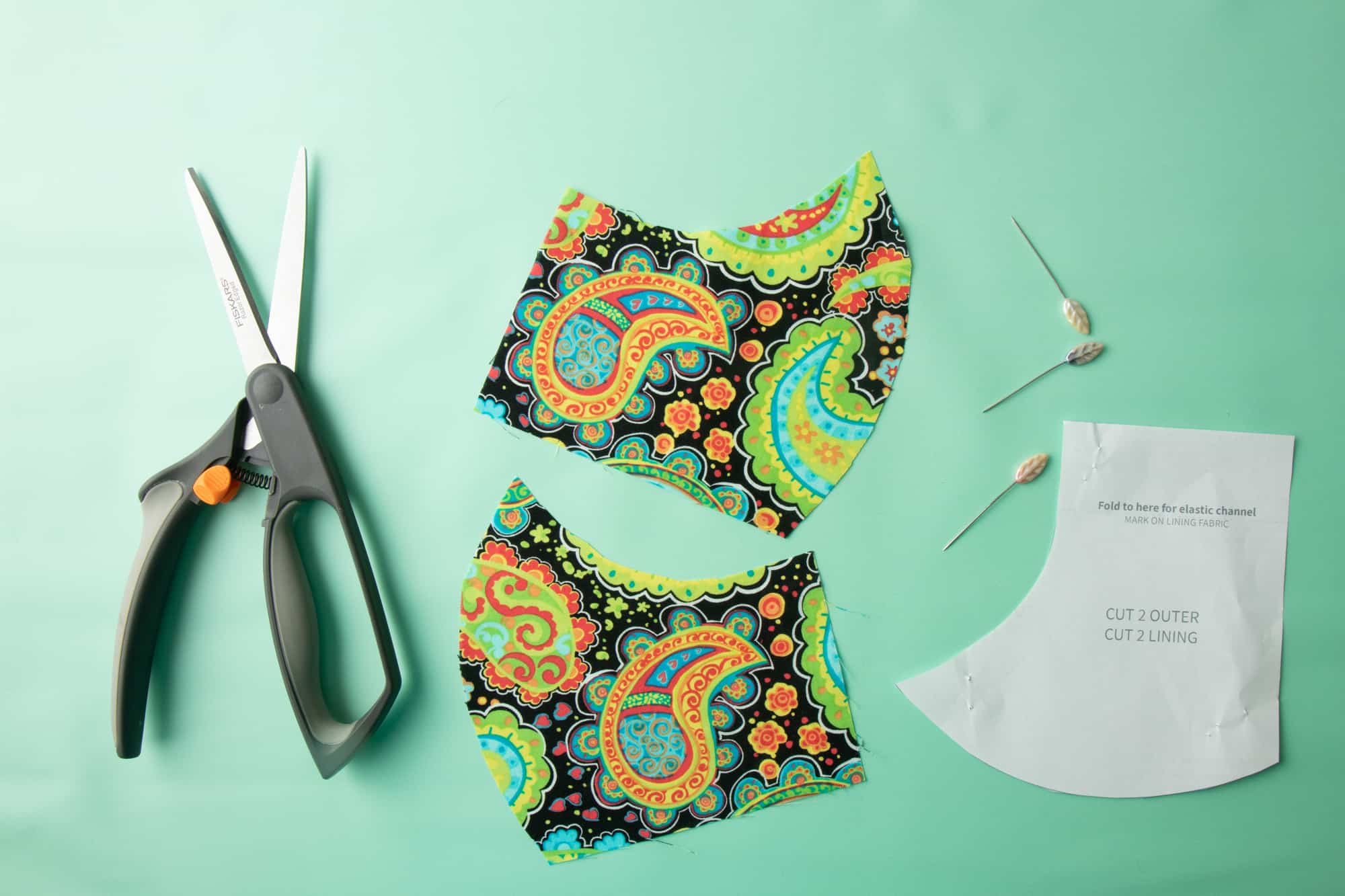 Scissors sit next to cut out fabric pieces, paper pattern pieces, and pins.