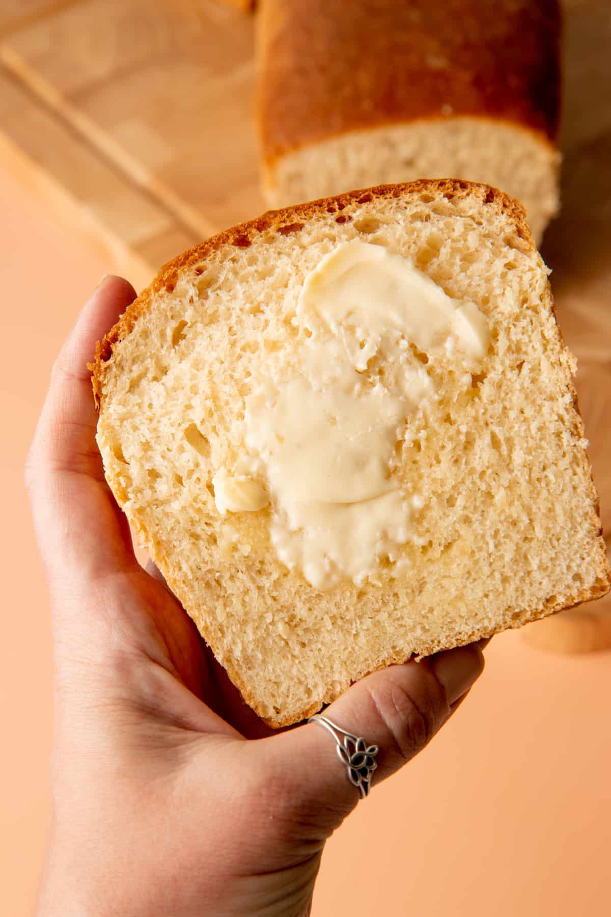 Hand holds a piece of bread slathered in a butter.