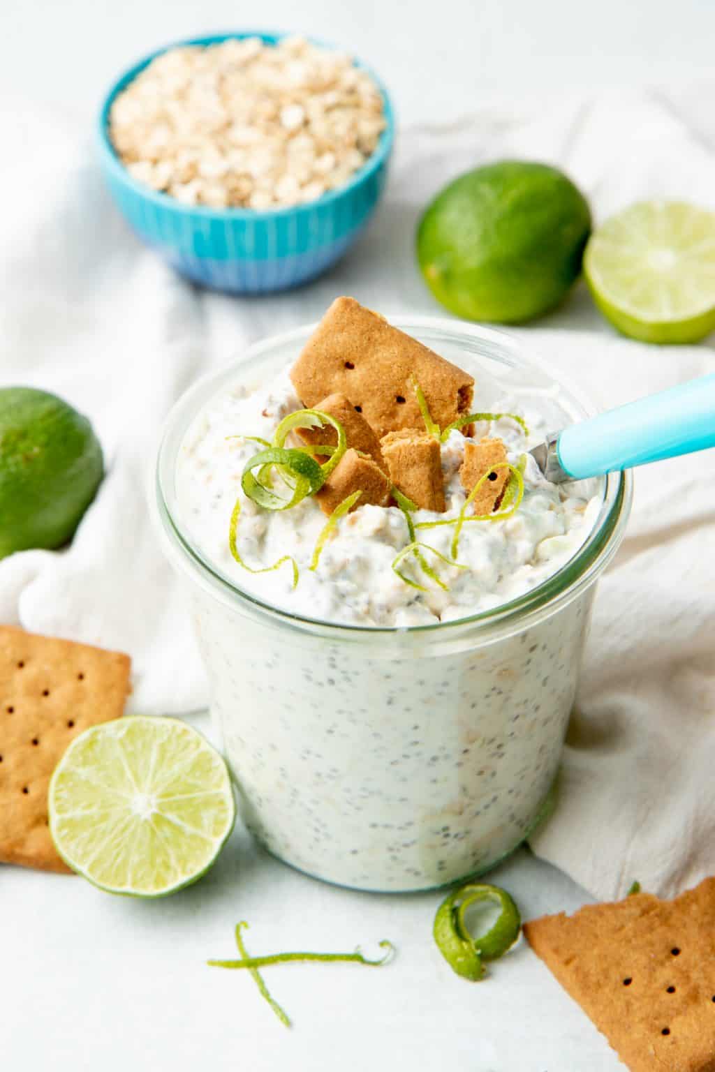 A small glass jar is filled with overnight oats and topped with graham cracker and lime twists.