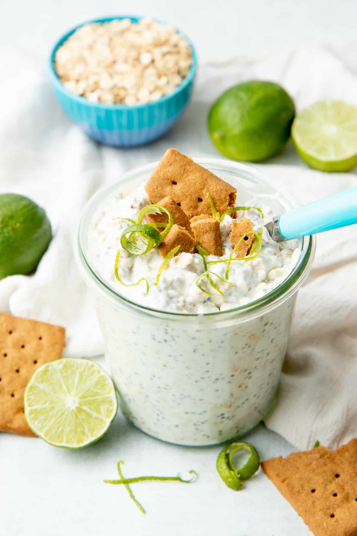 A small glass jar is filled with overnight oats and topped with graham cracker and lime twists.