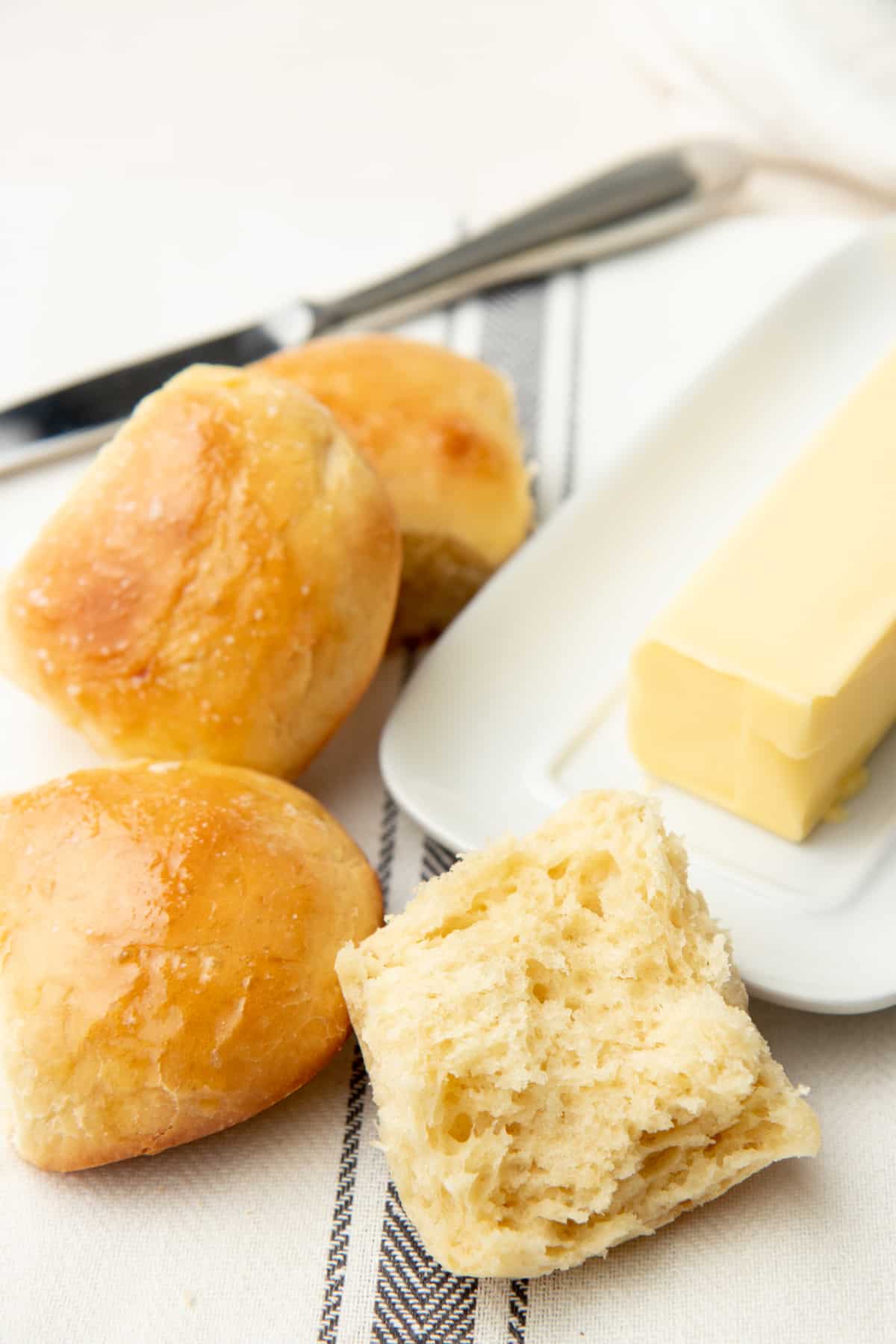 A cut roll sits next to whole rolls and a dish of butter.