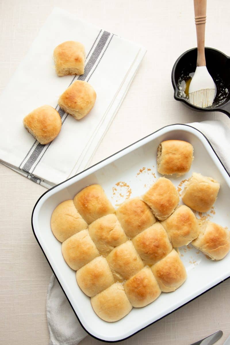 A pan filled half with bread rolls. Three rolls sit on a cloth napkin in the left hand corner.