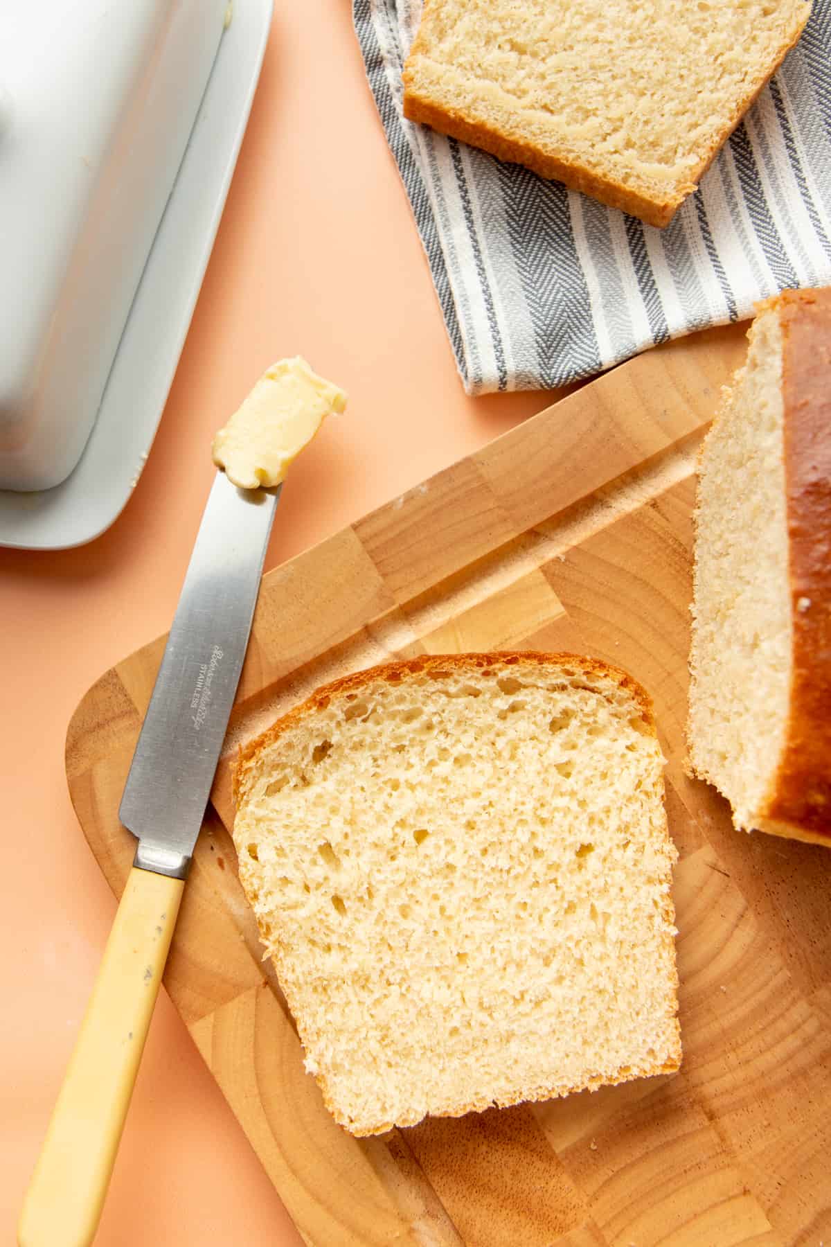 A slice of bread sits on a wooden cutting board next to a knife covered in butter.