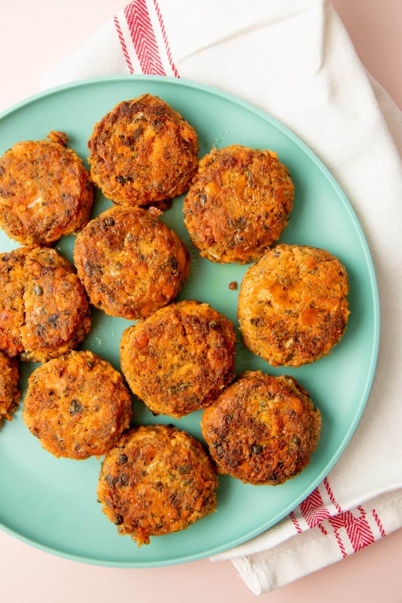 A teal plate filled with salmon cakes sits on a pink and white dish cloth.