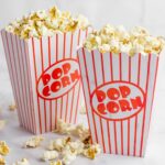 Two red and white striped boxes of popcorn overflowing with kernels in a kitchen