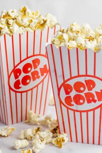 Two red and white striped boxes of popcorn overflowing with kernels in a kitchen