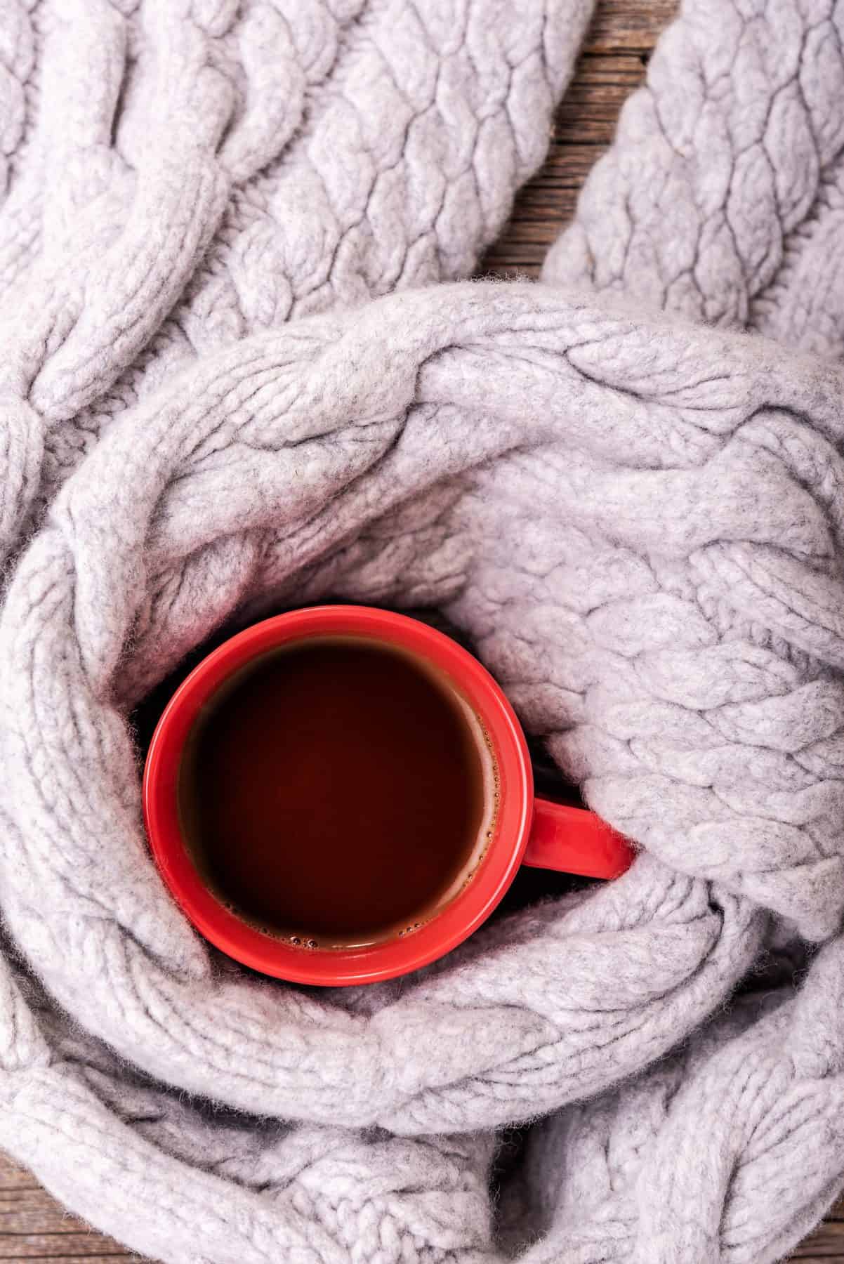 A scarf is wrapped around a red cup full of tea.
