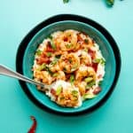 A bowl of Paleo Shrimp and Grits sits on a teal background. Cayenne peppers sit off to the side.