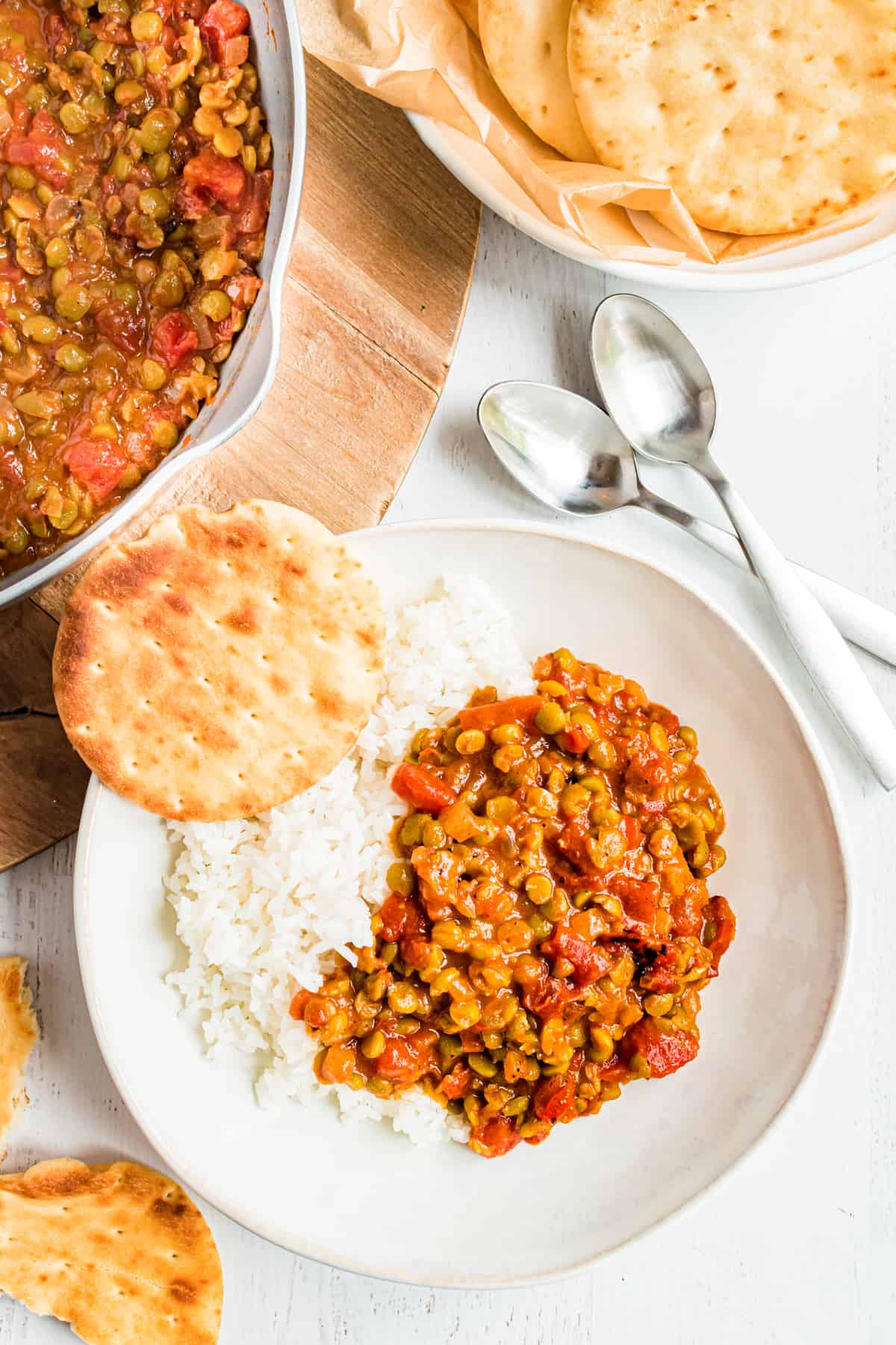 A bowl of split pea curry sits surrounded by naan bread.