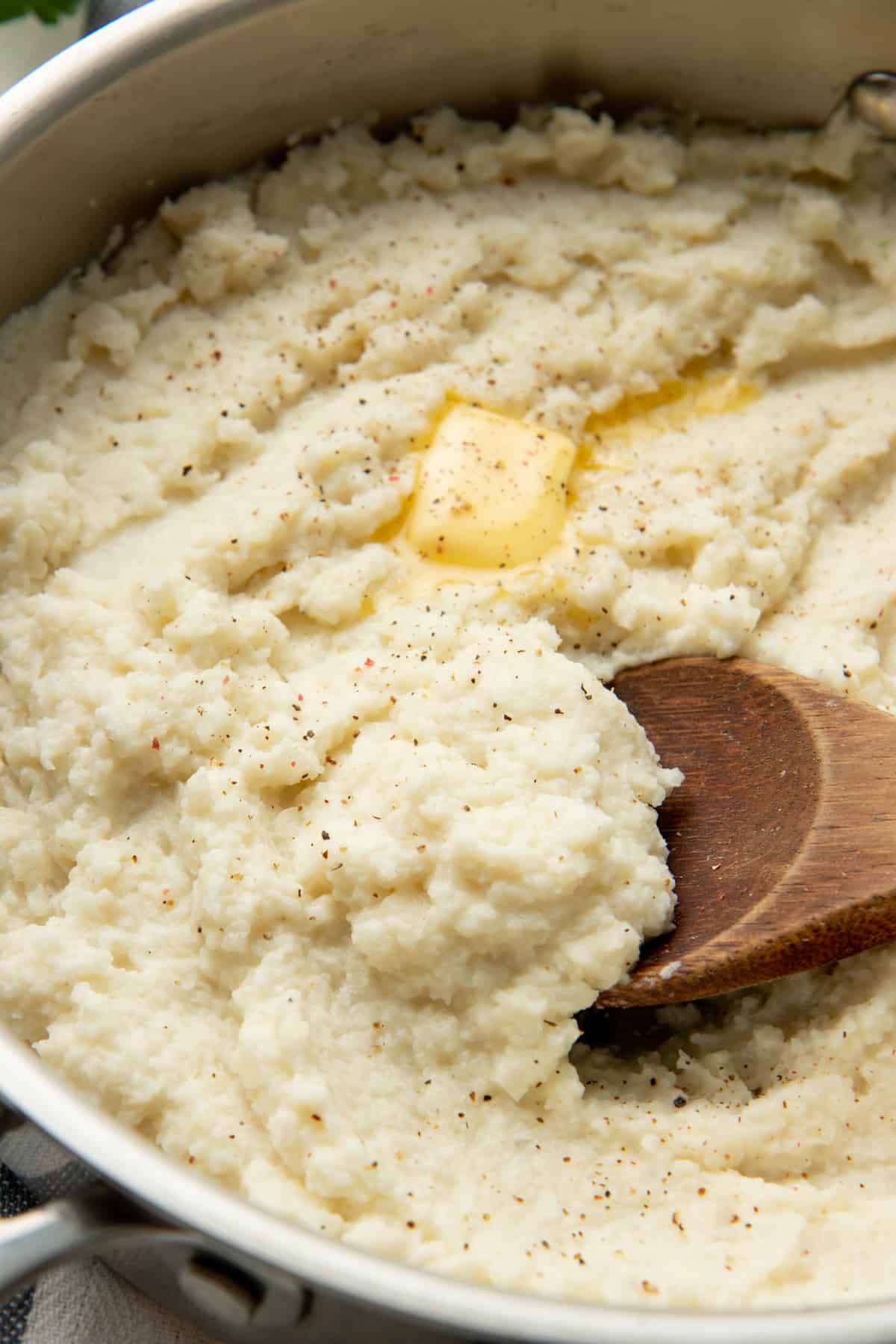A wooden spoon mixes cauliflower grits in a large pot.
