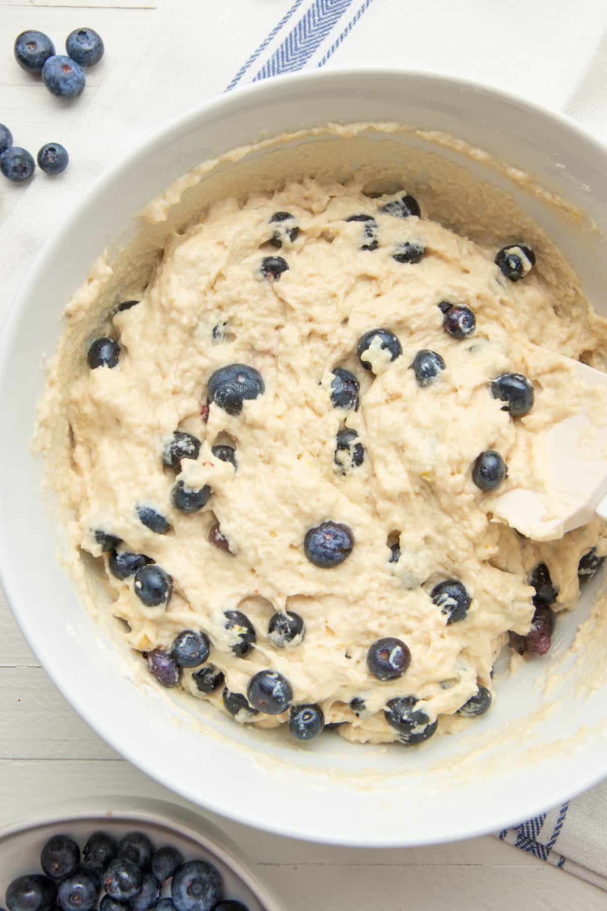 A spoon mixes fresh blueberries into muffin batter.