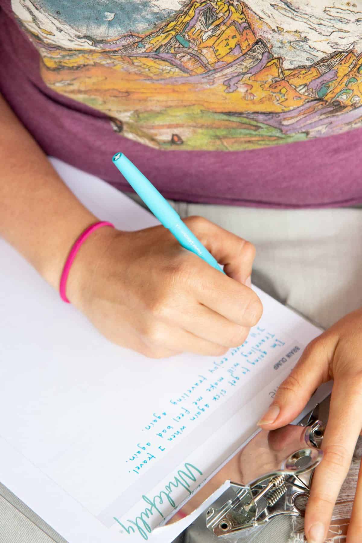 A hand writes on a piece of paper with a blue pen.