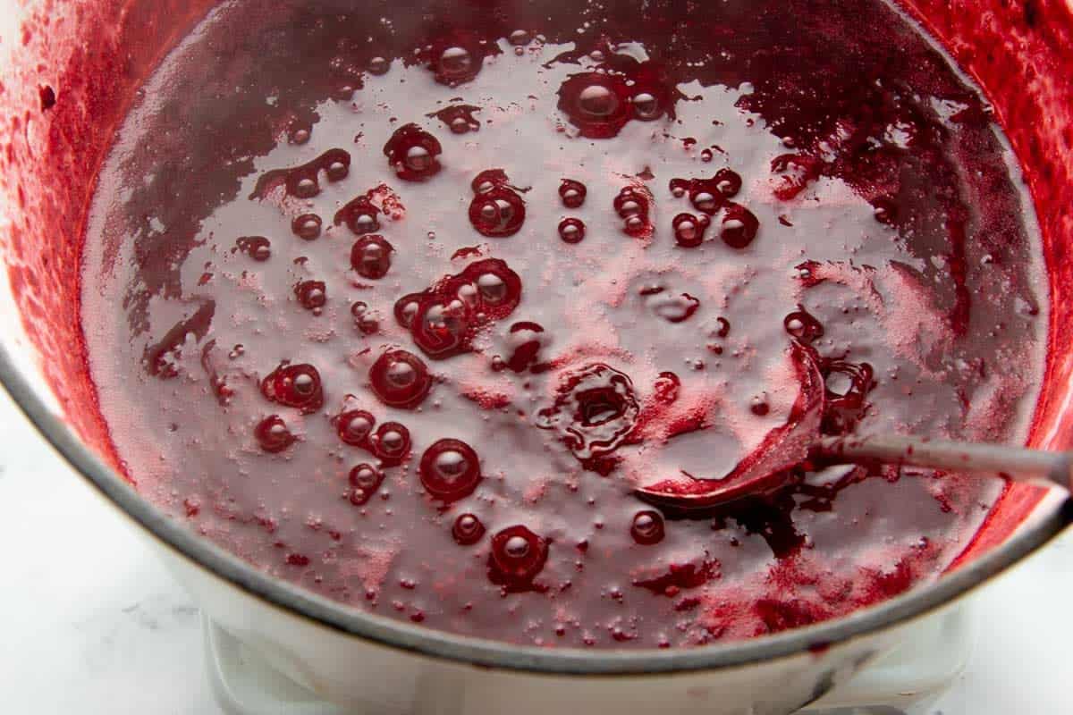 Close-up of boiling mixed berry puree in pot with spoon.